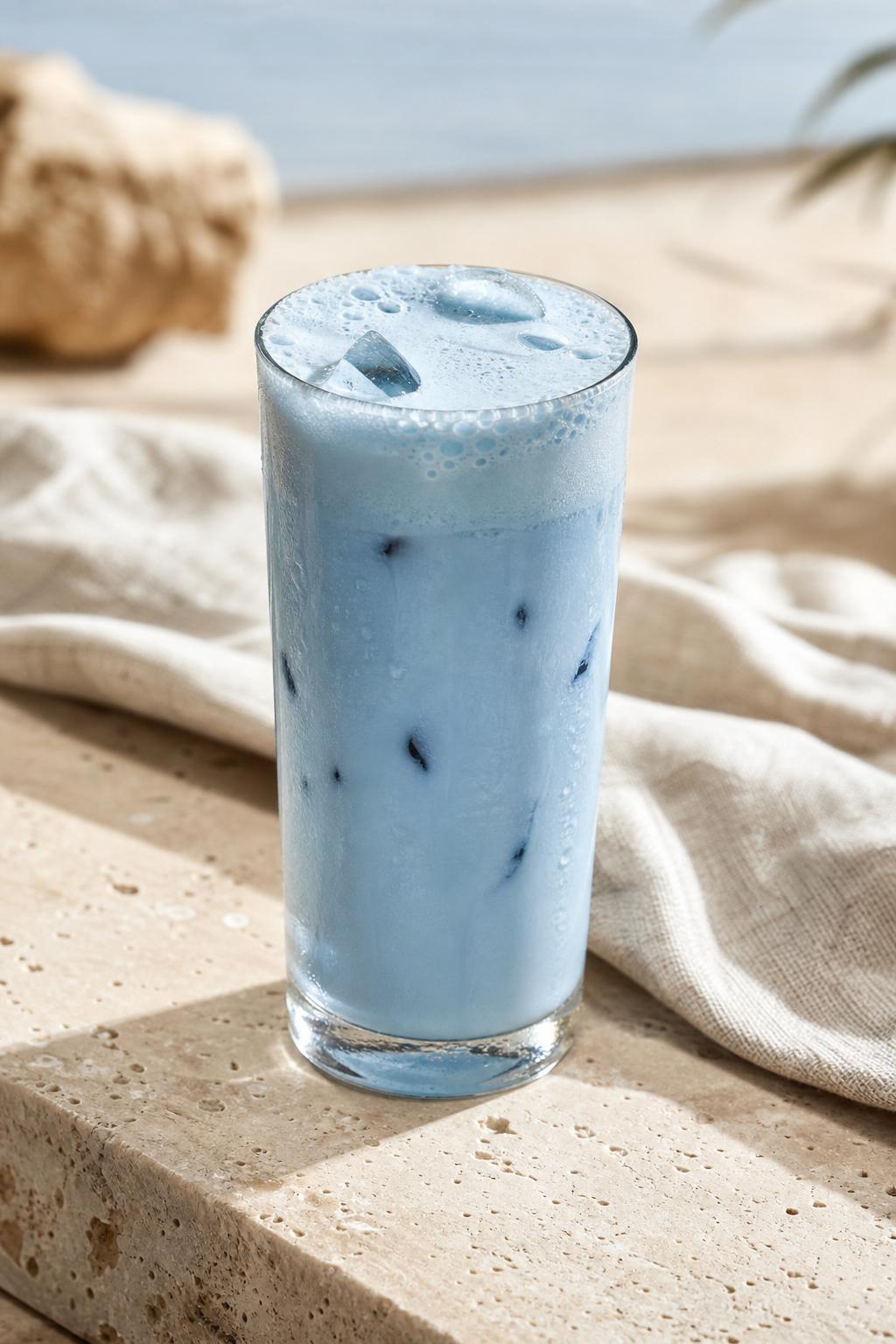 Un grand verre de blue latte glacé BLUA, crémeux et photoréaliste, sur une surface beige lumineuse
